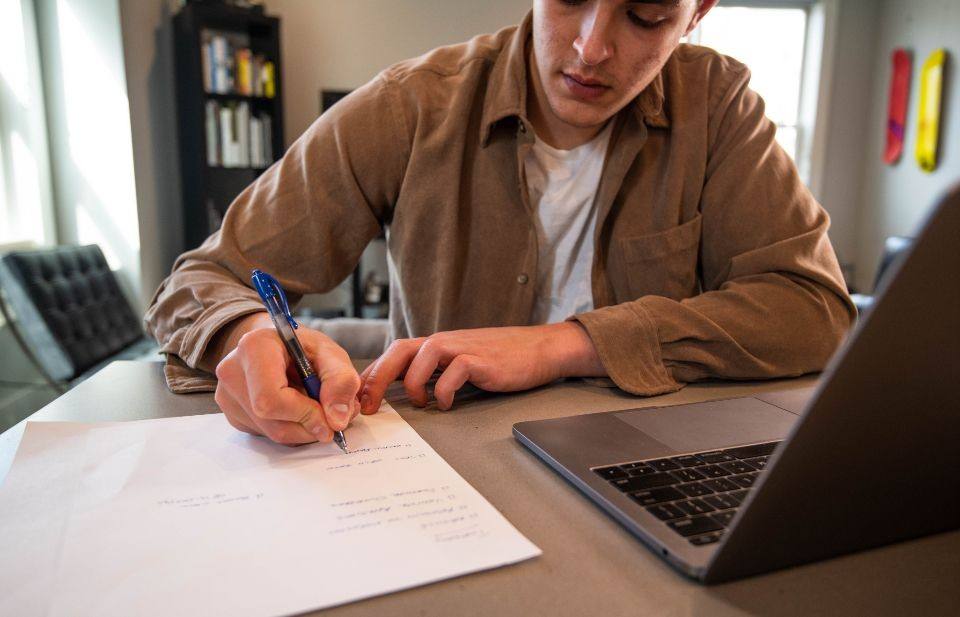 Man schrijft op papier naast een laptop