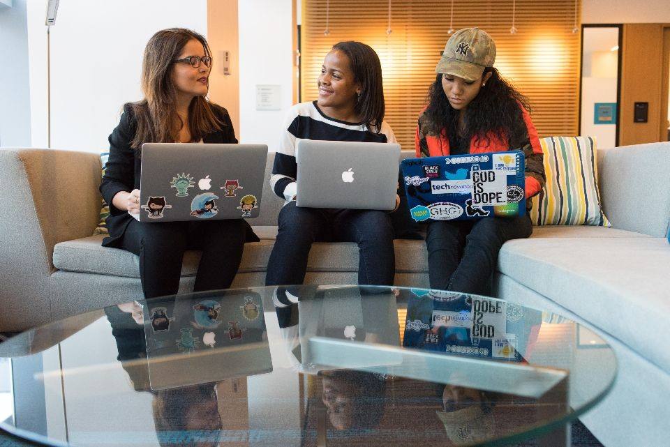 Drie vrouwen zitten samen op een bank met hun laptops